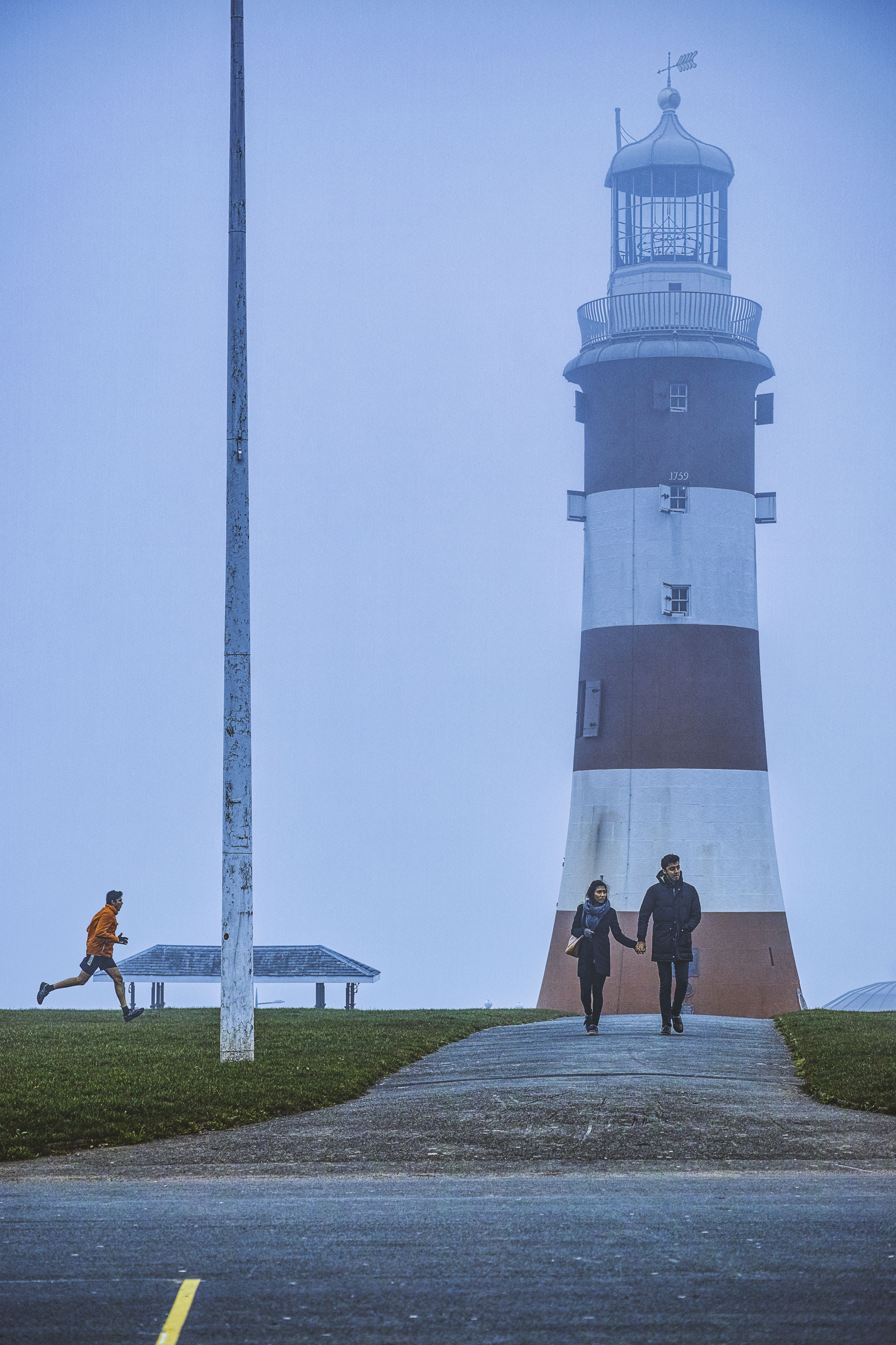 Jogger and couple in front of a foggy Smeatons Tower on Plymouth Hoe